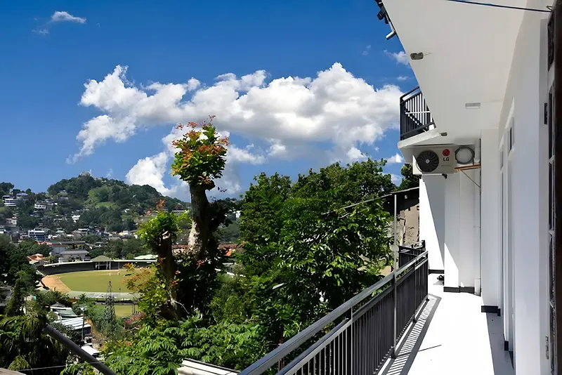 Balcony at Cozy Homestay Kandy looking out over green hills, rooftops and a cricket ground under a blue sky