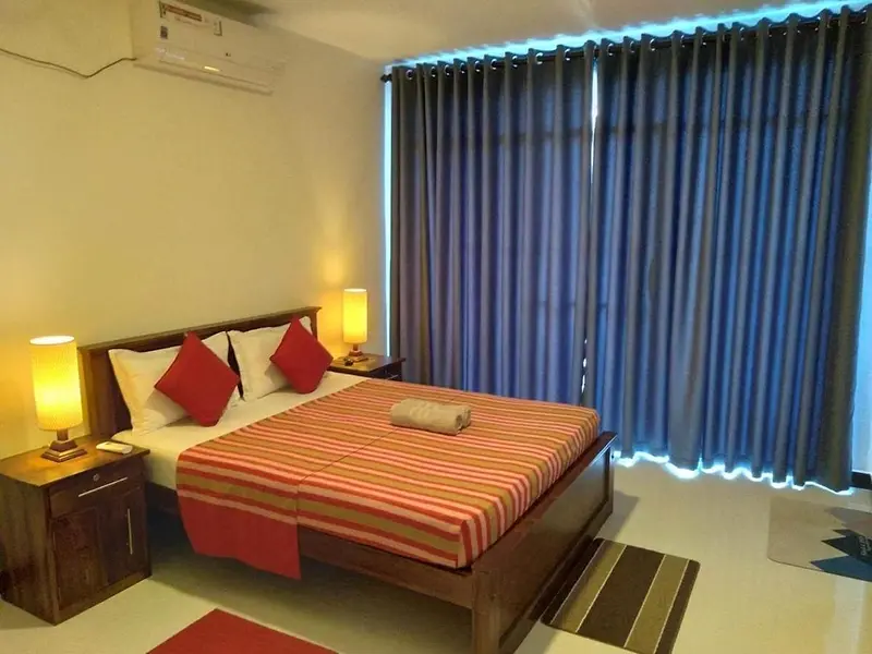Double bed with red cushions and a striped throw by tall blue curtains