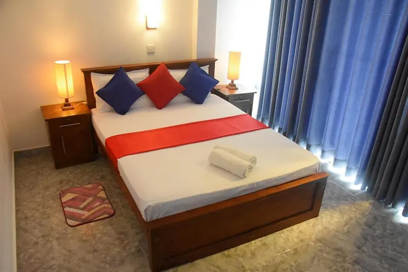 Double bed with blue and red cushions by sunlit curtains