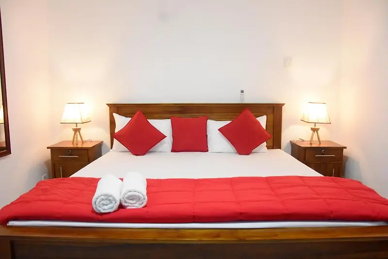 Double bed with red cushions and teak bedside tables in a bright room at Cozy Homestay Kandy